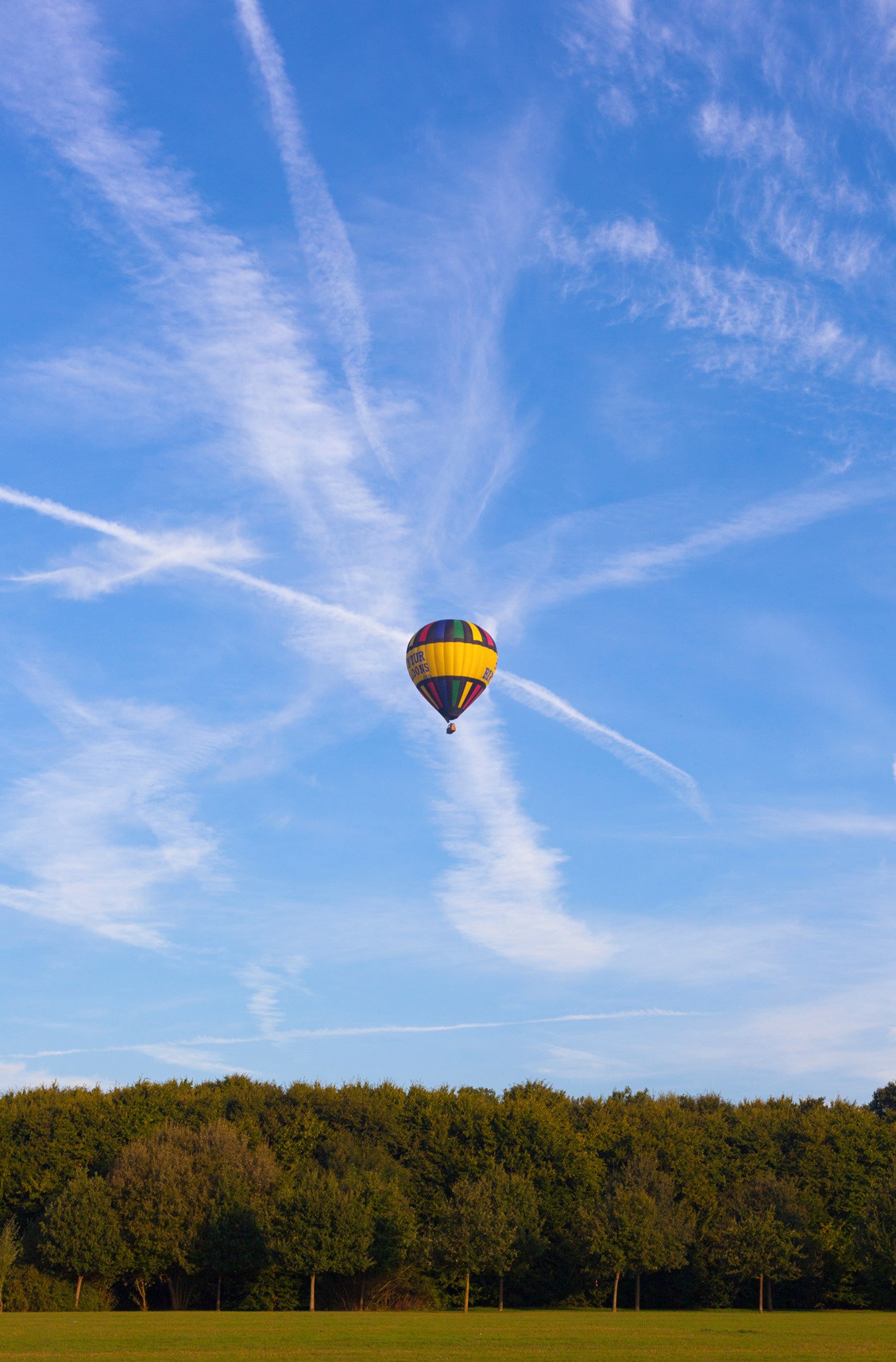 Condensation trails from aircraft flying from Luton airport criss cross the sky behind our Happy Birthday balloon as it takes off on a balloon flight from Fairlands Valley in Stevenage, Hertfordshire in 2019.