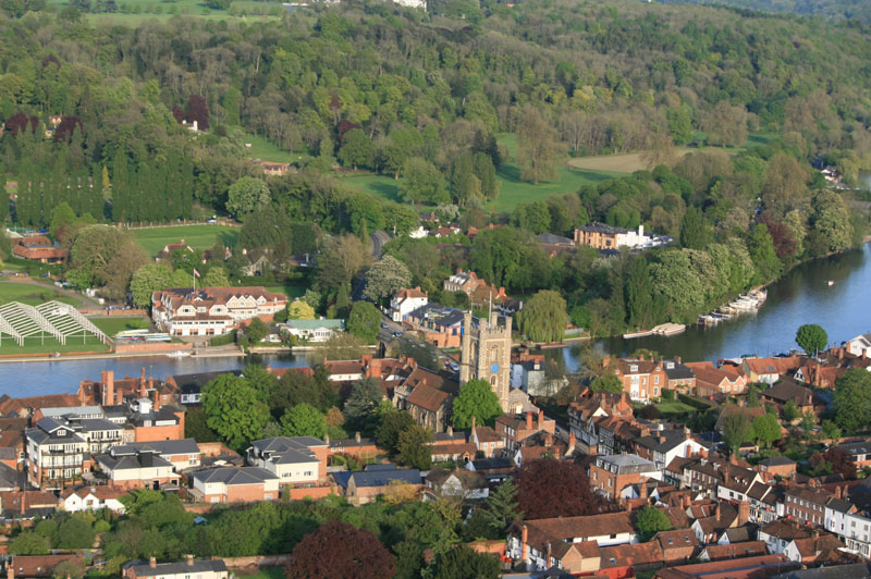 Clearly visible in this fine aerial view of Henley on Thames is the Church of St Mary the Virgin, an important landmark dating back to the 12th and 13th centuries. To the right of the church the white building is the Angel Inn which is one of many hotels in Henley if you are making a weekend break and the two buildings sit either side of the river bridge which takes you east to the Leander Club and the Henley Regatta grounds. In this picture preparation for the regatta with the framework for large marquees can be seen.