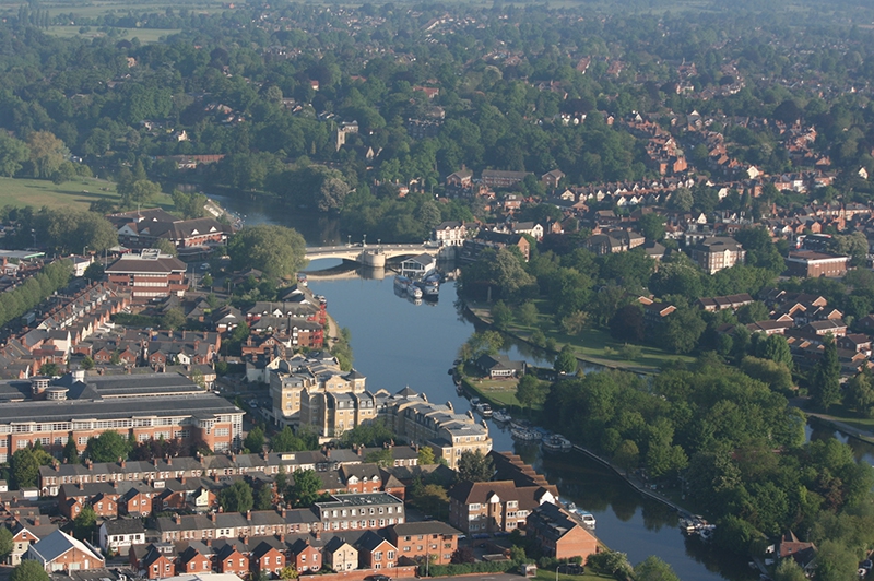 Caversham Bridge aerial picture with little activity on the river or the bridge and the river very calm and providing a great reflection of the buildings and trees alongside the river because this was a balloon flight in the early morning. Built in 1926 it was opened by Edward Prince of Wales. There has been a bridge here over the River Thames since 1163.
